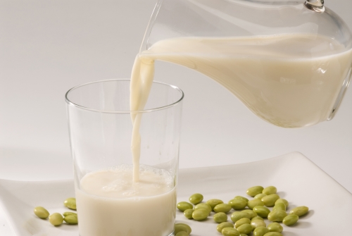 Soy milk pouring in a glass . Fresh soy beans in foreground. White background.